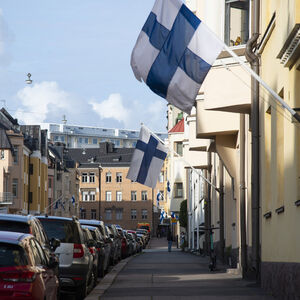 Talojen välissä on pitkä jono parkkeerattuja autoja. Jokaisen talon lippusalossa on Suomen lippu.