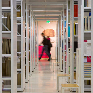 Krjaston hyllyjä joiden takana kulkee ihmisiä.