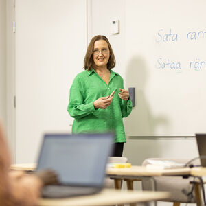 Teacher in front of the class. On white board it says "Sata rantaa. Sataa räntää."