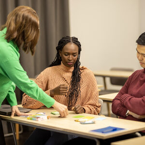 A teacher and two students are looking at a card game on the table.
