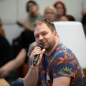 Yleisö kuuntelee miestä joka puhuu mikrofoniin.