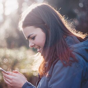 Ihminen katsomassa puhelintaan, tausta blurrattu. A person looking at their cellphone, blurry background.