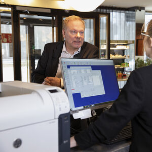 A person at a hotel reception desk talking to another person behind a computer. 