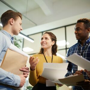 A group of people in a discussion, holding papers and folders in an office setting.