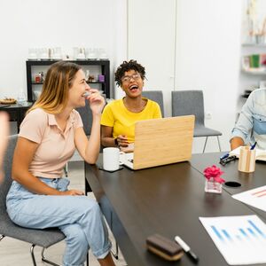 Kolme ihmistä kokouspöydän ääressä kannettavan tietokoneen ja asiakirjojen kanssa. Etualalla elehtivä henkilö.