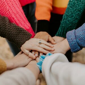 En grupp människor bildar en cirkel med sina händer staplade i mitten, klädda i färgglada tröjor.