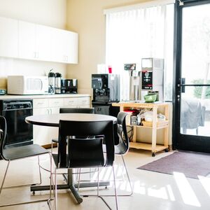 A break room with a table and four chairs, a kitchenette, coffee machine, microwave, and a glass door to the outside.