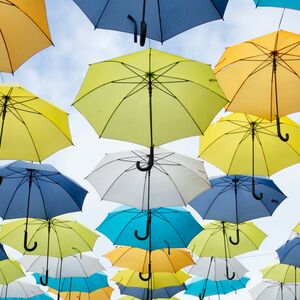 En grupp färgglada paraplyer hänger i luften mot en ljusblå himmel.