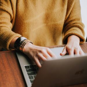 Person i gul tröja använder en bärbar dator på ett träbord.