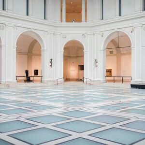 Rymlig museumsal med valv, vita väggar, statyer och målningar. Golvet har en geometrisk glasdesign.