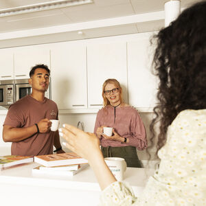Three people holding mugs, standing in a modern kitchen with white cabinets and books on the counter.