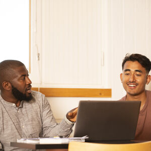 Kaksi henkilöä istuu pöydän ääressä kannettavan tietokoneen kanssa keskustelemassa valoisassa huoneessa.