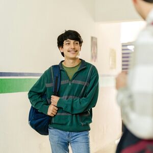 Two people with backpacks are in a hallway with green and blue stripes and posters on the wall.