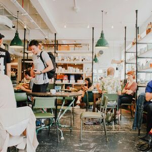 Folk sitter och pratar i ett livligt kafé med gröna stolar och hyllor fyllda med föremål i bakgrunden.