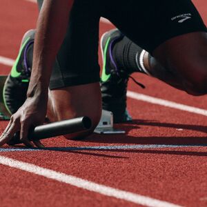 A sprinter in starting blocks holding a baton, ready to race on a red track.