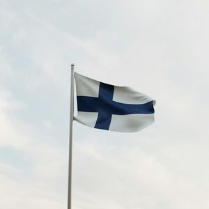 En finsk flagga med ett blått kors på en vit bakgrund vajar på en flaggstång mot en molnig himmel.