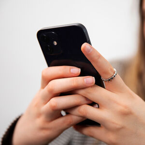 Lähikuva käsistä, jotka pitävät mustaa älypuhelinta.