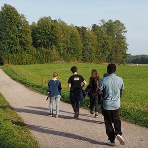 Viisi ihmistä kävelee polulla vehreän pellon halki aurinkoisena päivänä.