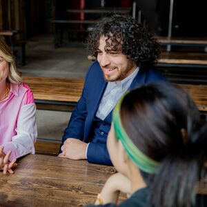 Neljä ihmistä istuu puisessa pöydässä keskustelemassa. Kaksi heistä on selin kameraan.