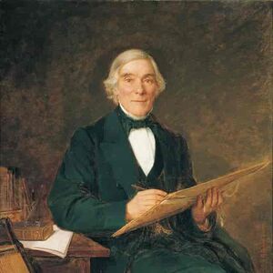 Mies tummassa puvussa istuu pöydän ääressä, pitää asiakirjaa, vierekkäin on soitin.