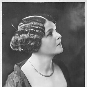 Mustavalkoinen muotokuva naisesta, jolla on nuttura, kaulakoru ja tumma mekko. Alareunassa allekirjoitus.