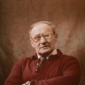 Henkilö, jolla on tummanpunainen paita kauluspaidan ja solmion päällä, kädet ristissä ja kello vasemmassa ranteessa.