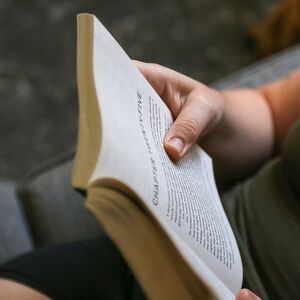 En person håller en öppen bok med text, liggande på en soffa.