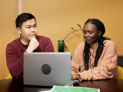 Nainen ja mies istuvat pöydän ääressä. Pöydällä on muistivihko ja tietokone.