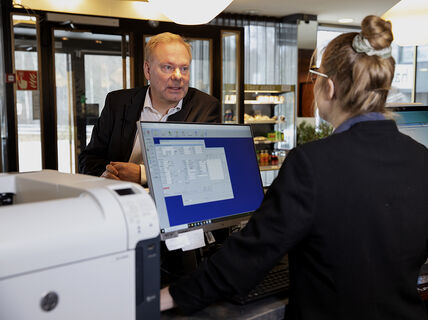 A person at a hotel reception desk talking to another person behind a computer. 