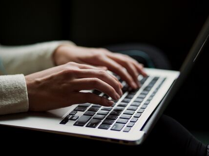 Lähikuva käsistä kirjoittamassa kannettavan tietokoneen näppäimistöllä.