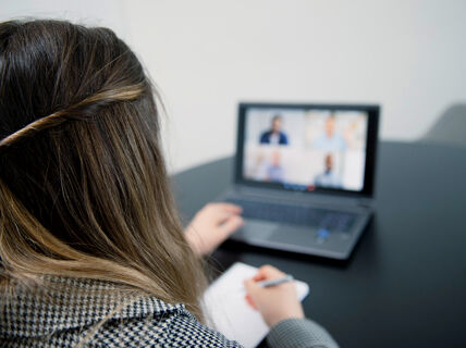 Woman with braided hair taking notes during a video conference on a laptop.