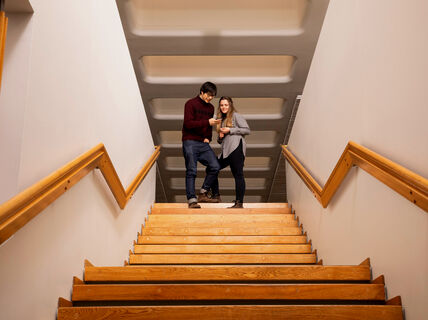 Två personer står längst upp i en trätrappa och pekar på en surfplatta. Trappan har träledstänger.