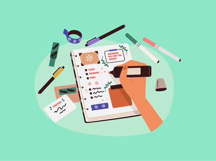 Käsi kirjoittaa kalenteriin, ympärillä on tusseja, tarroja ja teippiä vihreällä pinnalla.