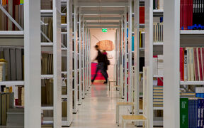 Library shelves with people walking behind them.