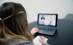 Pitkähiuksinen henkilö tekee muistiinpanoja videokonferenssin aikana.