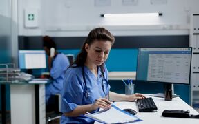 Två vårdpersonal arbetar vid skrivbord med datorer, den ena skriver och den andra talar i telefon.