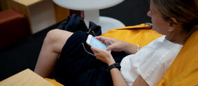 A woman is sitting in a beanbag and she is surfing on her mobile phone.