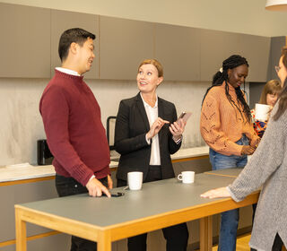 Ihmiset keskustelevat rennosti modernissa keittiötilassa, jossa on harmaa pöytä ja beige kaapit.