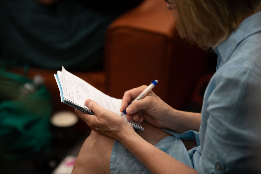 Henkilö kirjoittaa muistiinpanoja. Hänellä on kädessä muistivihko ja kynä.