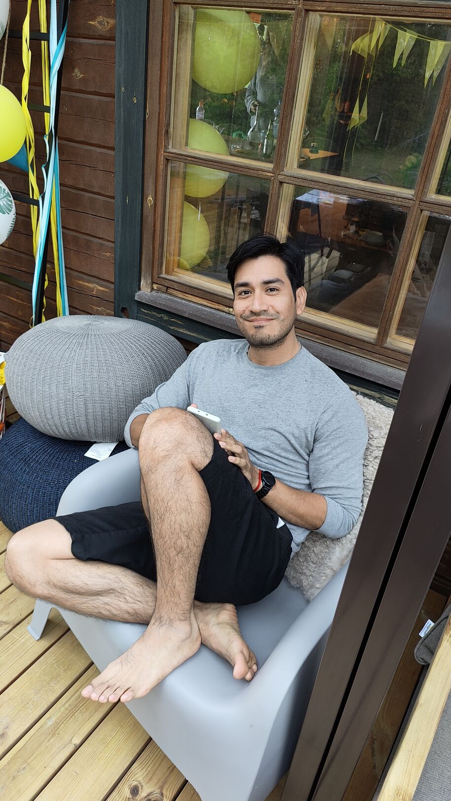 Jonathan sitter på en grå stol med benen korsade, håller en smartphone, med ballonger och band i bakgrunden.