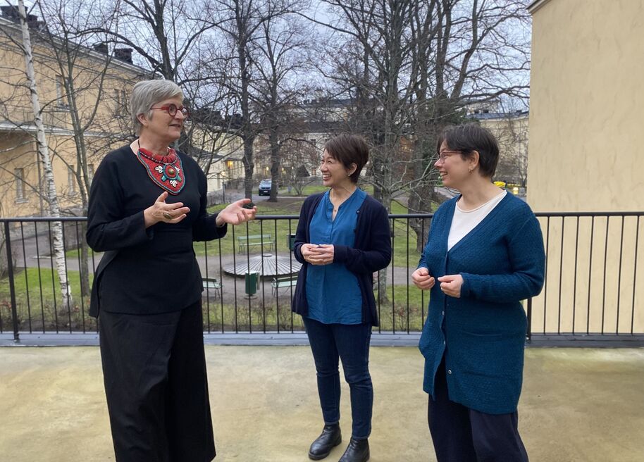 Kolme henkilöä seisovat keskustelemassa yliopistorakennuksen sisäpihalla.