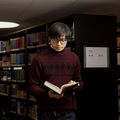 A young man is reading a book in a library.