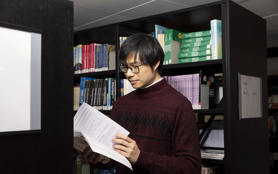 A young man is browsing a book next to a bookshelf in a library.