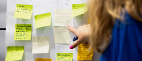 A person is pointing at post-it notes on a whiteboard.