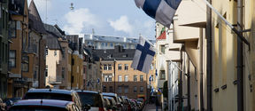 Talojen välissä on pitkä jono parkkeerattuja autoja. Jokaisen talon lippusalossa on Suomen lippu.