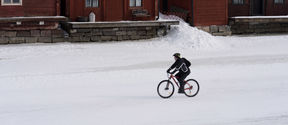 A cyclist cycling past old wooden houses in winter.