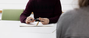 A person is sitting at a table and holding a pen.
