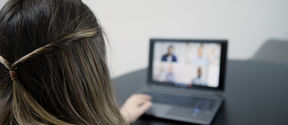 A person is using a laptop. A video conversation appears blurred on the laptop.