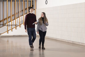 Two students are walking in the corridor. They are smiling.